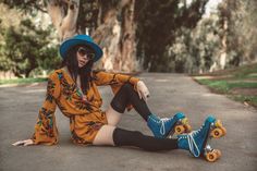 a woman sitting on the ground with her legs crossed, wearing blue roller skates