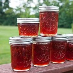 four jars filled with red pepper jelly sitting on top of a wooden table next to grass