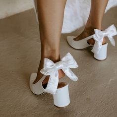 a close up of a person's feet wearing white shoes with bows on them