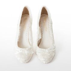 a pair of white wedding shoes with bows on the toe and lace detailing, against a white background