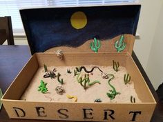 an open cardboard box filled with desert and cactus toys on top of a wooden table