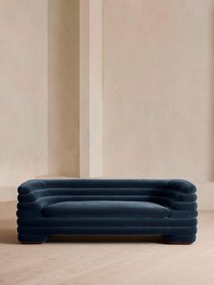 an upholstered blue couch sits in front of a beige wall and wooden floor