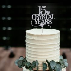 a white cake with greenery on top and the words crystal years written on it