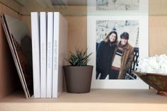 a bowl of white flowers sitting on top of a shelf next to books and a potted plant