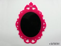 a pink mirror on a white wall in the shape of a frame with an ornate design