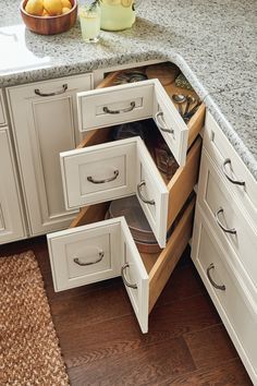 an open cabinet drawer in a kitchen next to a bowl of fruit on the counter