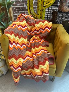 a crocheted blanket sitting on top of a yellow chair next to a cactus