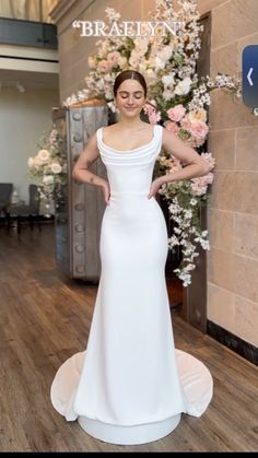 a woman standing in front of a flower display wearing a white dress and posing for the camera