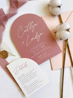 the wedding stationery is laid out on top of pink envelopes and cotton flowers