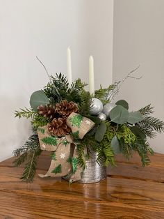 a christmas centerpiece with pine cones, greenery and candles on a wooden table