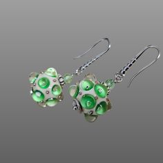 two green and white glass beads are hanging from silver earwires on a gray background