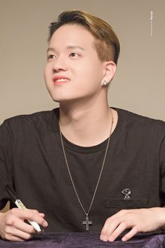 a young man sitting at a table with a cell phone in his hand and wearing a cross necklace