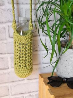 a crocheted bag hanging from the side of a brick wall next to a potted plant