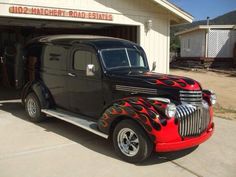 an old black and red car parked in front of a garage with flames on it