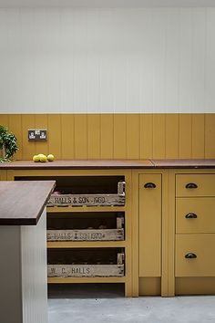 an empty kitchen with yellow cabinets and wooden counter tops on the island in front of a potted plant