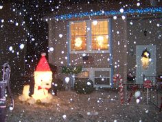 a snow covered yard with a house and christmas lights in the background at night time