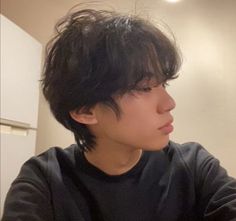 a young man with black hair sitting in front of a white refrigerator holding a cell phone to his ear