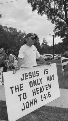 a man holding a sign that says jesus is the only way to heaven