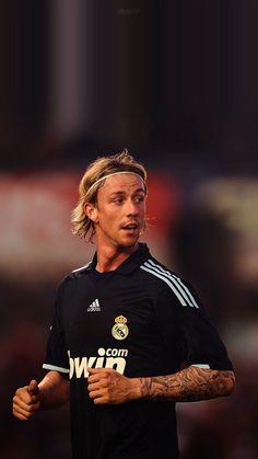 a man with long hair wearing a black shirt and holding a soccer ball in his hand