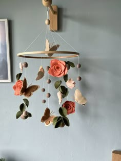 a mobile with flowers and leaves hanging from it's side on a wall next to a chair