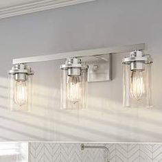 three light bathroom vanity fixture with clear glass shades and chrome finish, on a white wall