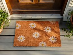 a door mat with white daisies on it sitting in front of a wooden door