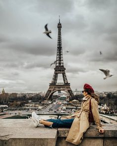 a woman sitting on top of a stone wall next to the eiffel tower