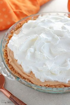 a pie with white frosting on top in a glass dish next to an orange pumpkin