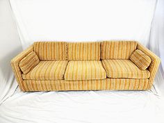 a yellow and white striped couch sitting on top of a white sheeted floor next to a wall