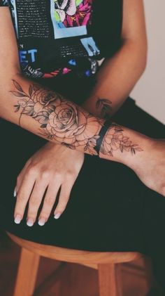 a woman sitting on top of a wooden stool with her arm covered in flowers and leaves