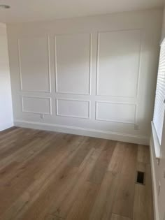 an empty room with white paneling and wood floors