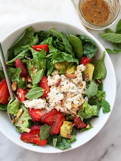 a salad with strawberries, cucumbers and nuts in a white bowl on a marble table