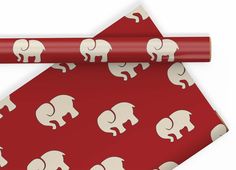 red wrapping paper with white elephants on it next to a rolled up gift wrapper