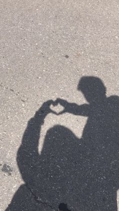 a shadow of a person making a heart with their hand on the ground in front of them