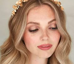 a woman with long blonde hair wearing a gold headband and flowers in her hair