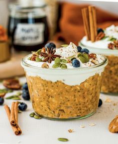 two small glass jars filled with food on top of a white table next to cinnamon sticks