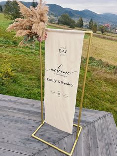 a wedding sign on a wooden deck in front of a grassy field with mountains behind it