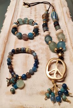 "This beautiful Set is part of my Peace, Love and Happiness Collection. With hues of blue aqua, seafoam blue, teal, accented with neutral tones strung onto a Genuine Leather Coffee Brown Cord: Handmade Necklace is 30\" long with a Peace Sign Pendant Focal bead, blue dragon vein Agate beads & Picasso rondelle multi-bead dangle. The One-of-a-Kind Necklace features stunning recycled beach glass, African Brass Focal bead on one side of the necklace and  an oval focal bead 40x19mm handmade ceramic with beautiful tones of Blue, Green & Aqua on the other side. All stones are accented with either African Ashanti Beads, Batik bone saucers, wavy flower rhinestone rondelle spacers and brass African beads. Wear it alone or layer it as shown on the second picture.  This listing is for 1 Necklace and 2 Handmade Blue Aquamarine Bracelets, Handmade Turquoise Aquamarine Bracelets, Turquoise Aquamarine Beaded Bracelets With Natural Stones, Spiritual Turquoise Aquamarine Jewelry, Spiritual Aquamarine Turquoise Jewelry, Bohemian Aquamarine Jewelry In Turquoise, Bohemian Turquoise Aquamarine Jewelry, Bohemian Aquamarine Turquoise Jewelry, Bohemian Aquamarine Jewelry