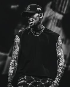 a black and white photo of a man with tattoos on his arm, wearing a baseball cap