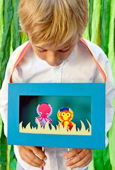 a young boy holding up a paper cutout with an octopus and monkey on it