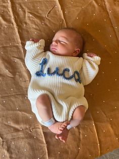 a baby laying on top of a bed wearing a sweater