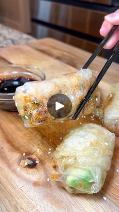 someone holding chopsticks over some food on a cutting board with dipping sauce in the background