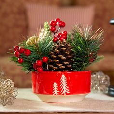 a red bowl filled with pine cones and berries on top of a table next to other christmas decorations