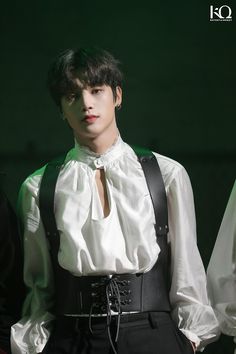 a male model with black suspenders, white shirt and dark pants is standing in front of a green background