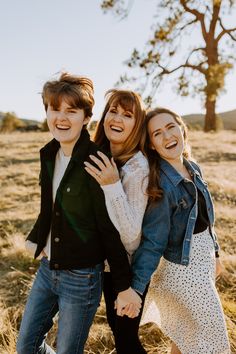 three young people standing in a field with their arms around each other and smiling at the camera