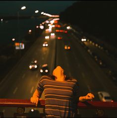 a woman leaning on a railing looking at the street lights from an overpass with cars driving down it