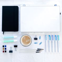 various office supplies laid out on a white surface with pens, markers and notebooks