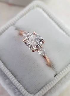 an engagement ring with three stones in it on a white cloth box that is sitting on top of a table