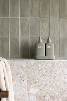 two bottles of soap sitting on top of a bathroom counter next to a towel rack