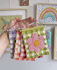 a person holding up four small crocheted purses in front of pictures on the wall